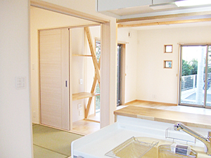 株式会社あいホーム:畳スペースでお昼寝する赤ちゃんと、リビングで遊ぶお子さんの様子を見ながらキッチンで家族の為のお料理作り